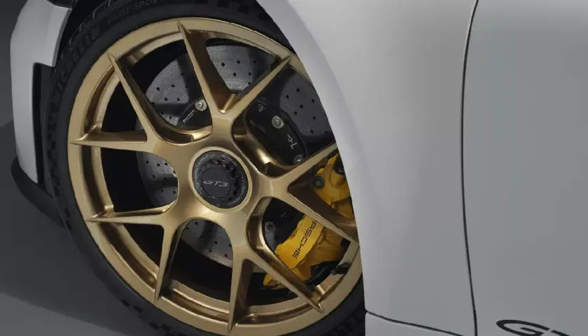 Detalle de un coche deportivo blanco con llantas doradas y pinzas amarillas. Se aprecian los discos de **frenos cerámicos** perforados, listos para la acción.