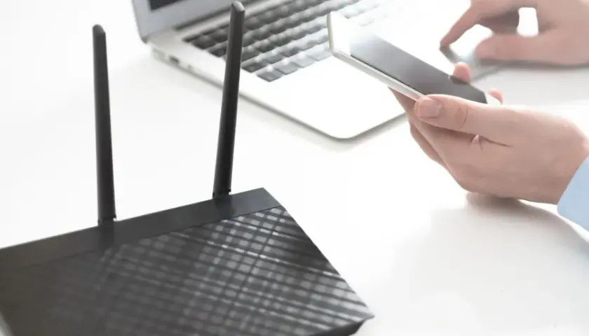 Osoba trzyma smartfon obok laptopa i routera, pokazując, jak udostępnić internet z telefonu na komputer przez USB.