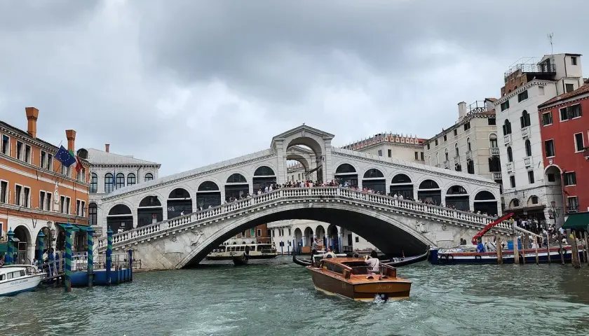 Un taxi venise navigue sur le Grand Canal, passant sous le célèbre pont du Rialto, bordé de bâtiments colorés.