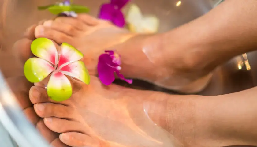 Piedi immersi in acqua con fiori colorati, suggerendo un momento di relax e benessere, forse legato alla riflessologia plantare stomaco.