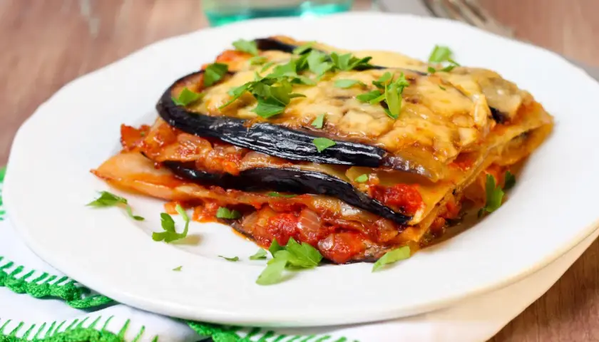 Deliciosa lasaña de berenjena, capas de berenjena, salsa de tomate y queso fundido, espolvoreada con perejil fresco.