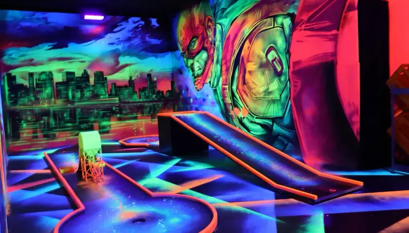 Neon-beleuchtete Bahnen und eine Skyline-Kulisse laden zum **Glow Minigolf** ein. Ein Superheld wacht über das Spiel.