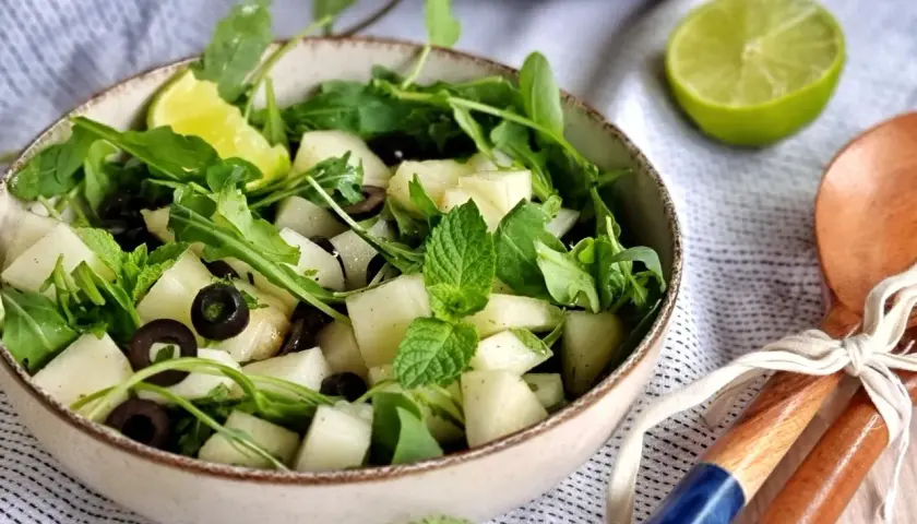 Refrescante ensalada de melón con rúcula, aceitunas negras y menta. Un toque de lima realza su sabor.