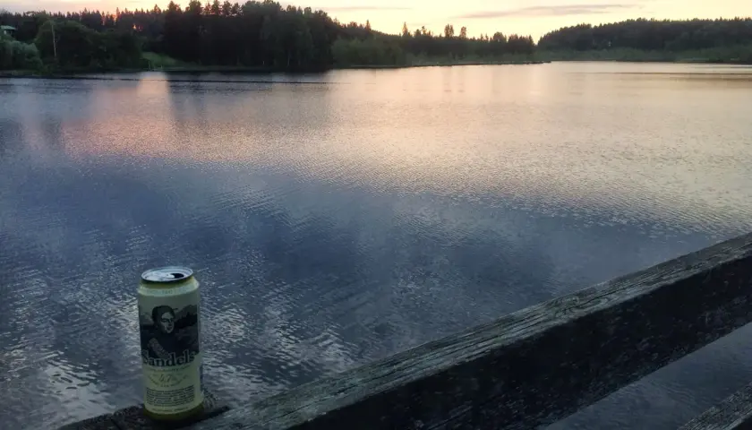 Une canette de bière Sandels, une bière karhu, repose sur un vieux bois au bord d'un lac paisible au coucher du soleil.