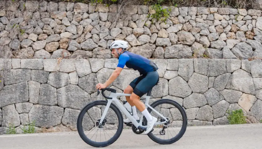 Ciclista pedaleando por una carretera en Mallorca en bici, con un muro de piedra detrás.