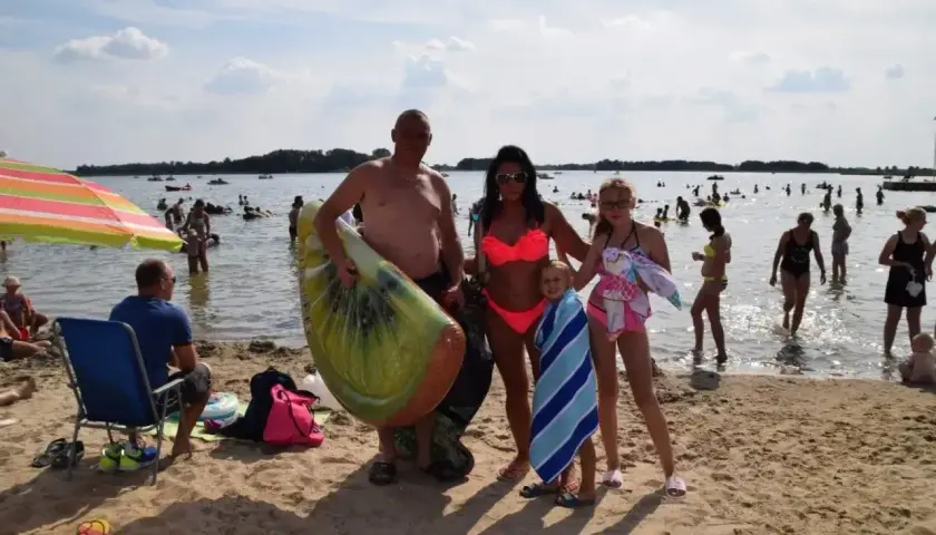 Rodzina na plaży nad jeziorem Niedzięgiel, z dmuchanym arbuzem i ręcznikami, cieszy się słonecznym dniem.