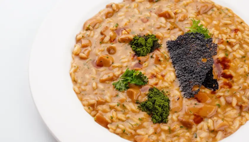 Risotto z grzybami i zieloną posypką na białym talerzu.