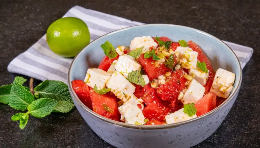 Erfrischender Wassermelone Feta Salat mit Minze und Pinienkernen, garniert mit Limettenabrieb. Ein leichter Genuss.