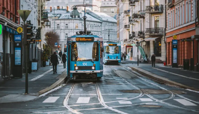 Niebieskie tramwaje na ulicy w Oslo, z budynkami po bokach.