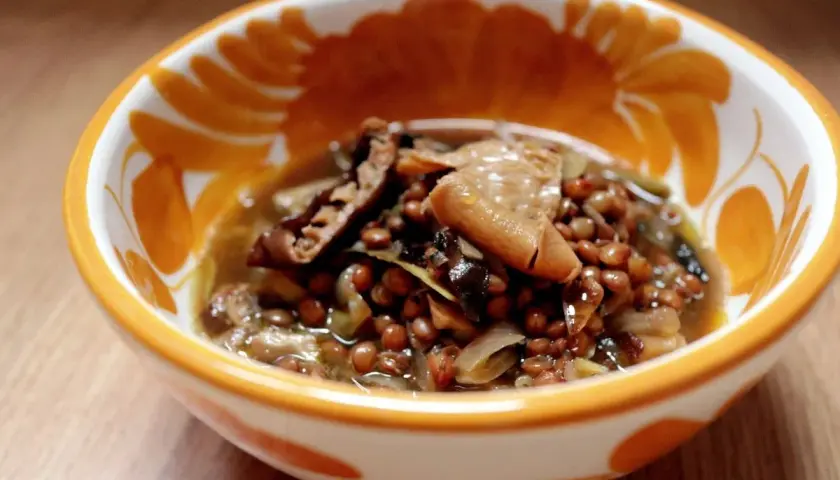 Un reconfortante plato de lentejas con boletus, servido en un cuenco decorado con motivos naranjas.