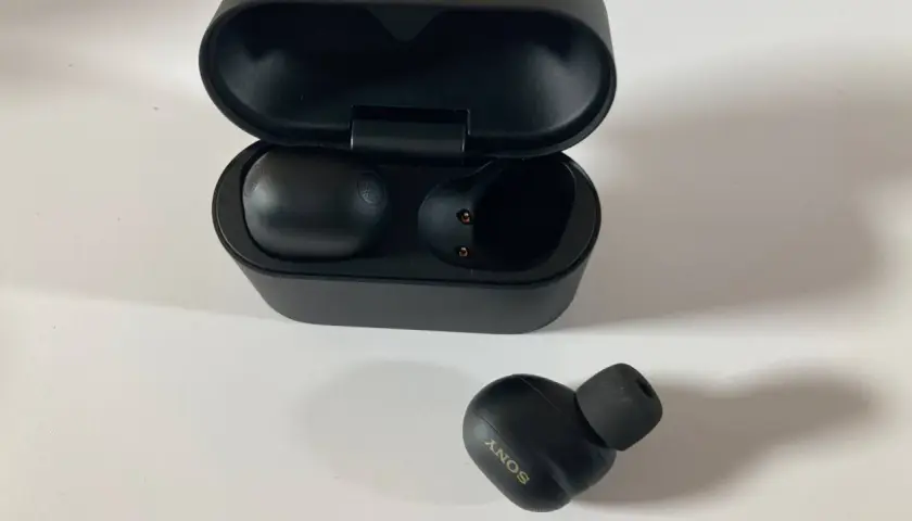 Schwarze Sony WF-1000XM6 Kopfhörer mit Ladecase. Ein Ohrhörer liegt daneben.