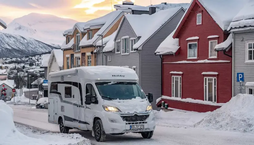 Un camping-car blanc roule dans une rue enneigée. Il semble être le camping-car le mieux isolé pour affronter le froid.