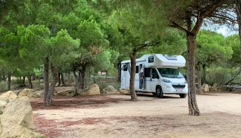 Un camping-car blanc est garé dans un endroit paisible, un spot camping-car sauvage, entouré de pins et de rochers.