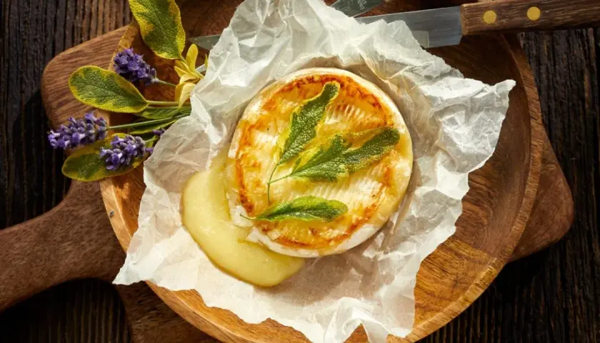 Camembert au barbecue, fondant et doré, servi sur papier sulfurisé avec des herbes aromatiques et des fleurs de lavande. Un délice à partager.