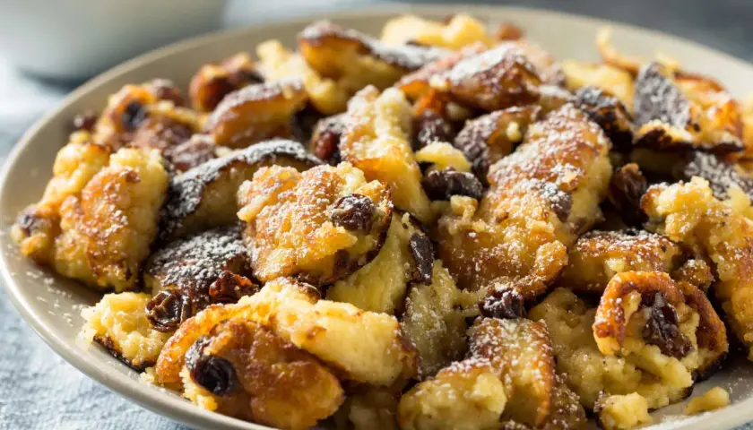 Ein Teller mit köstlichem, zerkleinertem Kaiserschmarrn, bestäubt mit Puderzucker und Rosinen. Eine leckere low carb Variante!