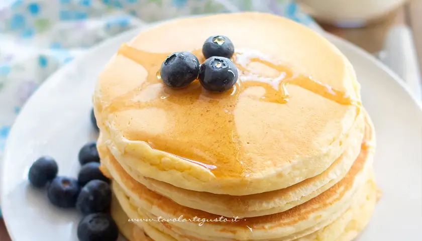 Pancake con albumi soffici e dorati, guarniti con mirtilli freschi e sciroppo d'acero.