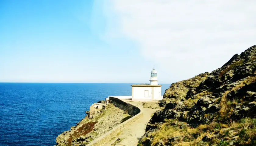 El faro de Cala Nans se alza sobre un acantilado rocoso, vigilando el azul intenso del mar Mediterráneo bajo un cielo despejado.
