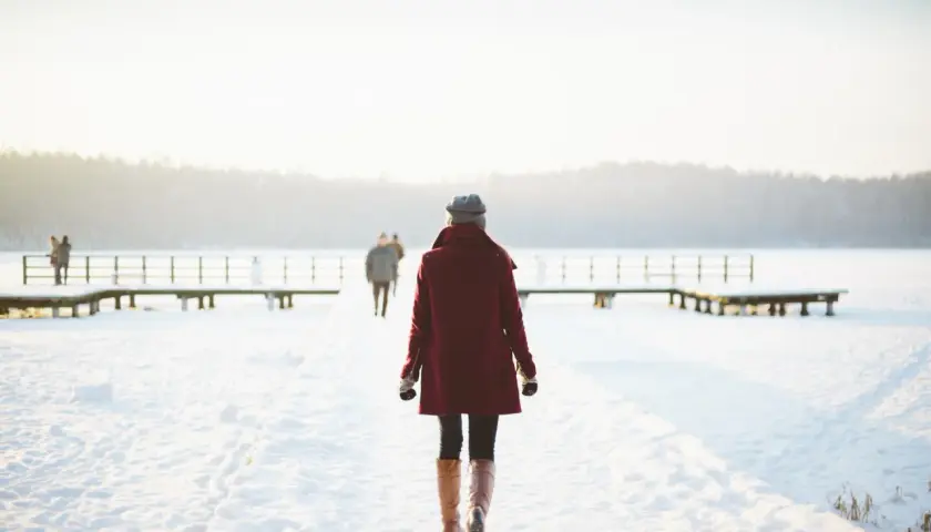 Kobieta w bordowym płaszczu idzie przez zaśnieżony teren, jakby uciekała od trudności, symbolizując nieumiejętność przyjmowania krytyki.