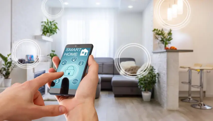 Dłoń steruje aplikacją "Smart Home" na telefonie, symbolizującą inteligentne życie i komfortowe mieszkanie.