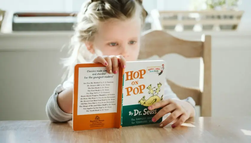 Dziewczynka czyta książki do czytania po angielsku, w tym "Hop on Pop" Dr. Seussa.