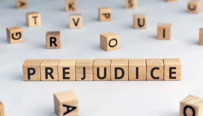 Des cubes en bois forment le mot "PREJUDICE", symbolisant le préjudice moral psychologique. D'autres lettres flottent autour.