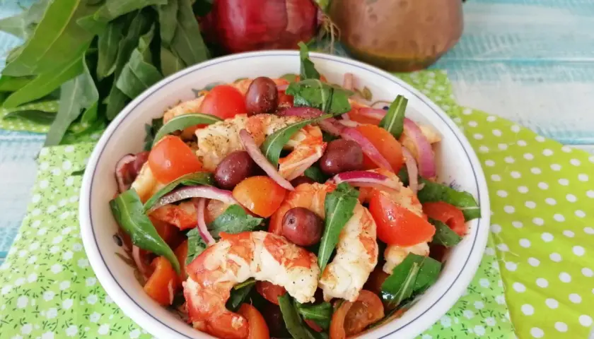 Deliziosa catalana di gamberi con pomodorini, olive, cipolla rossa e rucola, un piatto fresco e colorato.