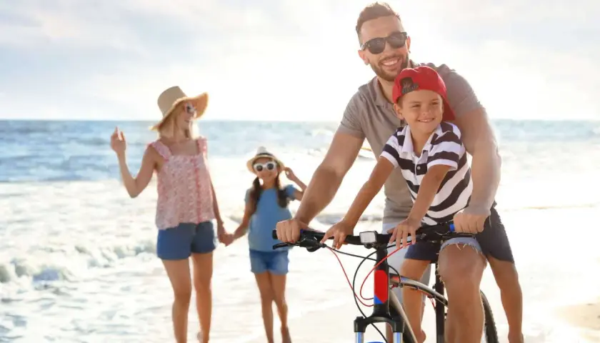 Famiglia felice in bicicletta sulla spiaggia, un'idea per le tue prossime idee viaggio con bambini in Italia.