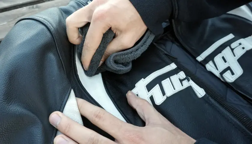 Manos limpian chaqueta de moto de cuero negro con detalles blancos. Aprende como lavar una chaqueta de moto.