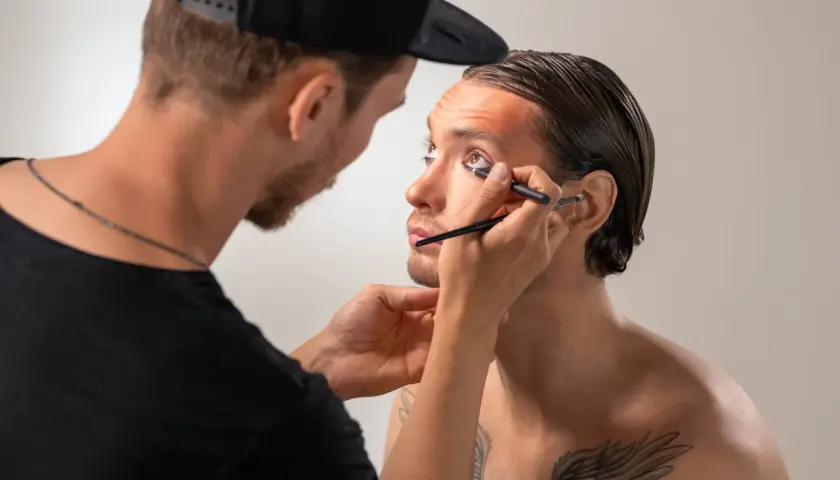Un truccatore applica l'eyeliner a un modello, creando un look audace.