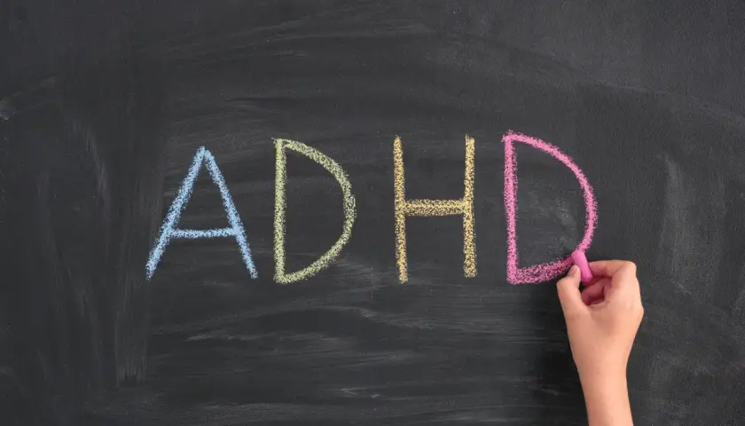 Napis "ADHD" kredą na tablicy, pisany przez rękę.