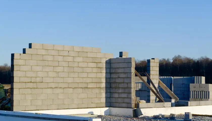 Budowa domu w toku. Wzniesiona ściana nośna z pustaków betonowych, widoczne fundamenty i materiały budowlane.