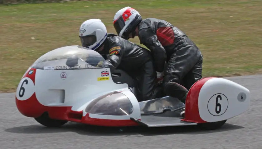 Dos pilotos en un sidecar de carreras, uno conduciendo y el otro en la silla lateral. El número 6 en el sidecar. William Dunlop, un nombre asociado con la velocidad.