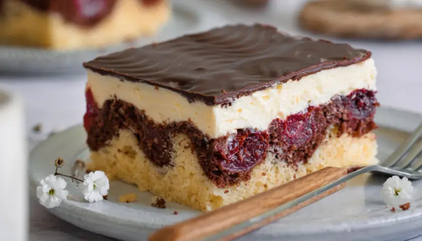 Ein Stück Donauwelle-Kuchen mit Schokoladenglasur, Sahne und Kirschen. Ein köstliches Rezept für den perfekten Genuss.