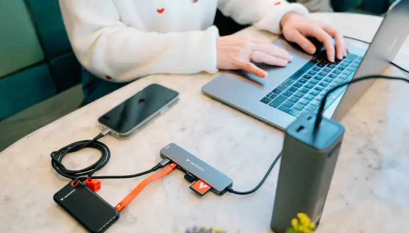 Kobieta pracuje na laptopie, podłączając telefon, dysk zewnętrzny i kartę SD do stacji dokującej USB 3.2.