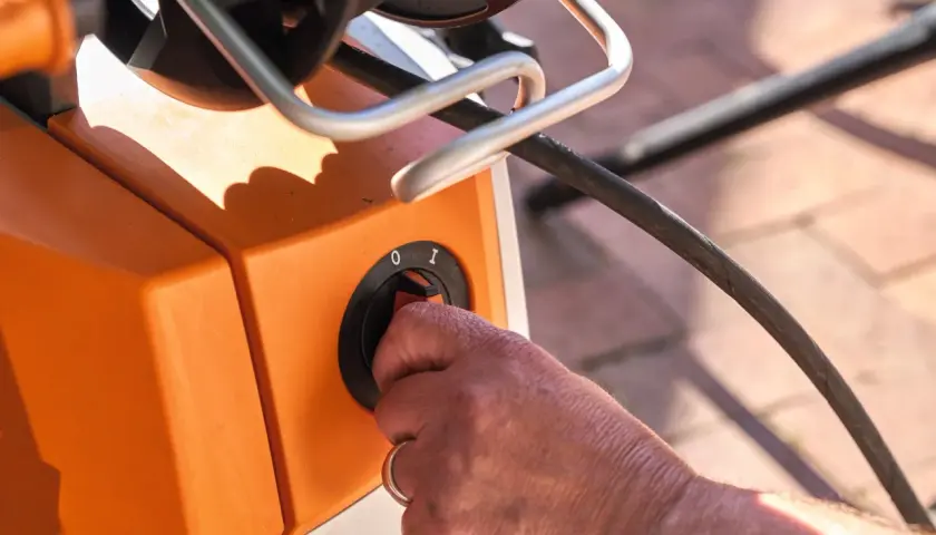 Hand dreht Schalter am orangefarbenen Hochdruckreiniger, bereit, ihn an den Wasserhahn anzuschließen.