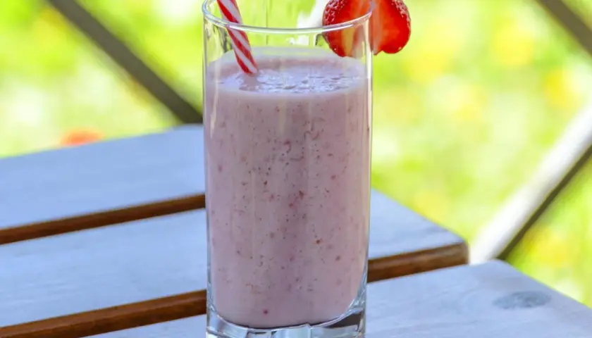 Orzeźwiający drink z truskawkami, udekorowany plasterkiem owocu, na drewnianym stoliku w letnim ogrodzie.