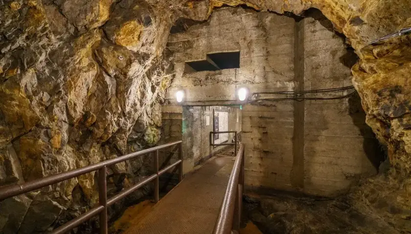 Tunel w podziemiach Walimia, z metalową kładką i poręczą, prowadzi do oświetlonego przejścia. Odkryj te niezwykłe walim atrakcje.