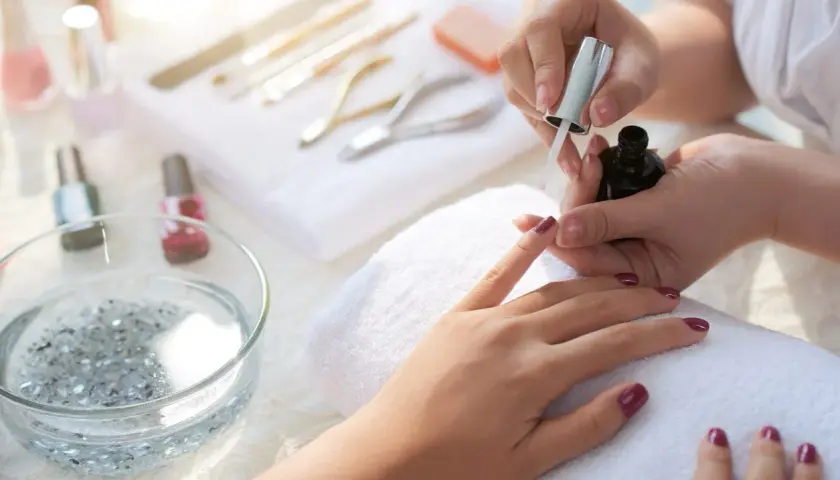 Manicure tytanowy krok po kroku: aplikacja lakieru na paznokcie, narzędzia do stylizacji w tle.