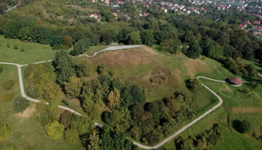 Widok z lotu ptaka na Kopiec Tatarski w Przemyślu, otoczony zielenią i wijącymi się ścieżkami. W oddali widać panoramę miasta.