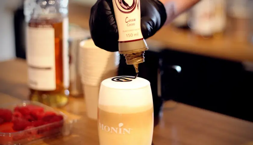 Barista ozdabia gorącą czekoladę do picia syropem kakaowym.