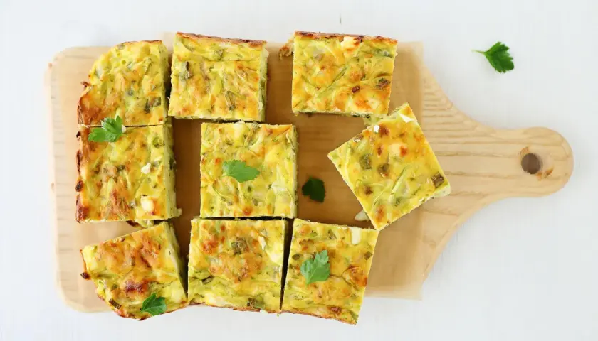 Pyszna frittata z cukinią pokrojona w kwadraty, ułożona na desce.