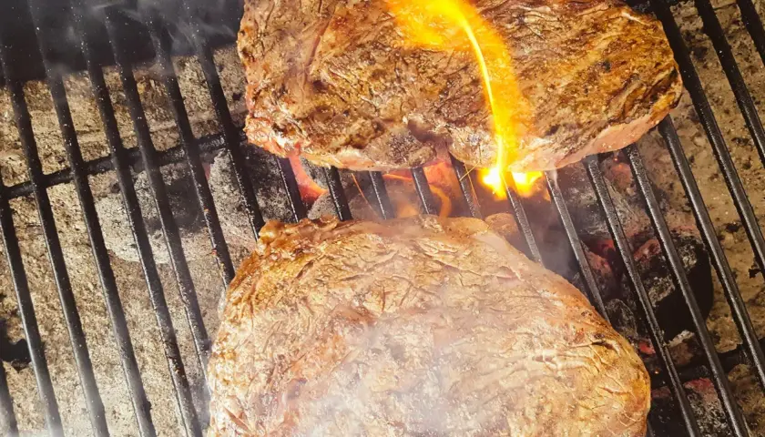 Två saftiga biffar grillas med ved. Flammor slickar köttet som får en perfekt yta.