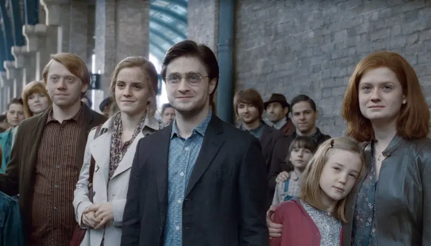 Harry Potter, z charakterystyczną blizną, stoi w tłumie na dworcu. Obok niego Hermiona i Ron.