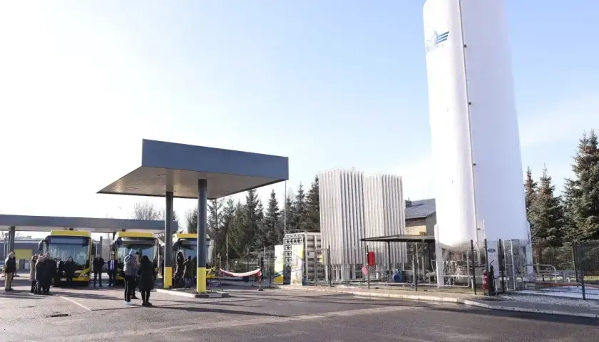 Stacja tankowania CNG. Żółte autobusy czekają pod wiatą, obok wysoki zbiornik i instalacja.