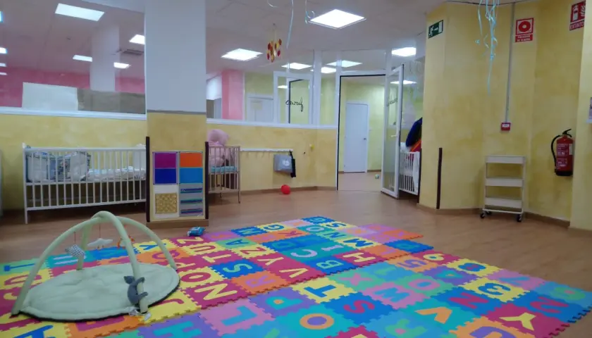 Un espacio acogedor en una escuela infantil o guardería, con cunas, alfombras de letras y juguetes para los más pequeños.