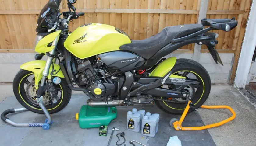 Moto Honda Hornet gialla pronta per cambiare l'olio di lubrificazione del motore. Attrezzi e olio a terra.