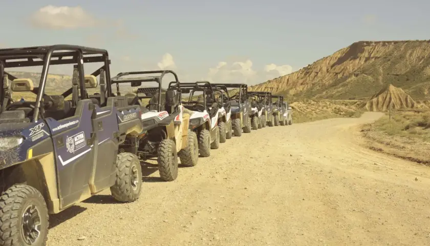 Una fila de vehículos todoterreno espera en un camino de tierra, listos para una aventura por el desierto, como si fueran un puente de todos los santos hacia lo desconocido.