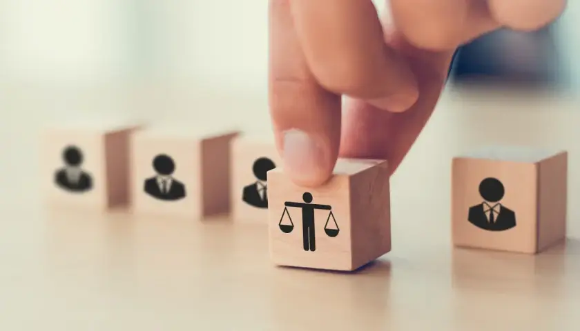 Dłoń układa kostkę z wagą sprawiedliwości obok kostek z ludzikami. To symbol tego, co daje członkostwo w partii: równość i reprezentację.