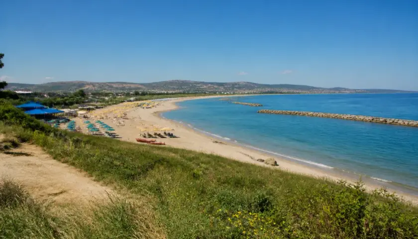 Plage de Pescara, Italie. Parasols bleus et jaunes, mer turquoise, digues en pierre, collines verdoyantes.