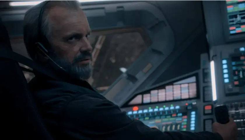 Un homme barbu, casque sur les oreilles, aux commandes d'un vaisseau spatial. L'avenir de l'humanité est en jeu dans For All Mankind saison 5.